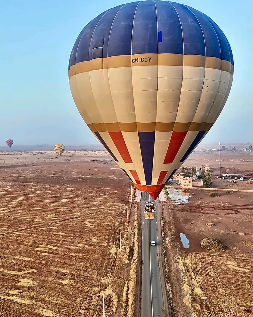 A balloon and its basket seen from the air above fields and a road