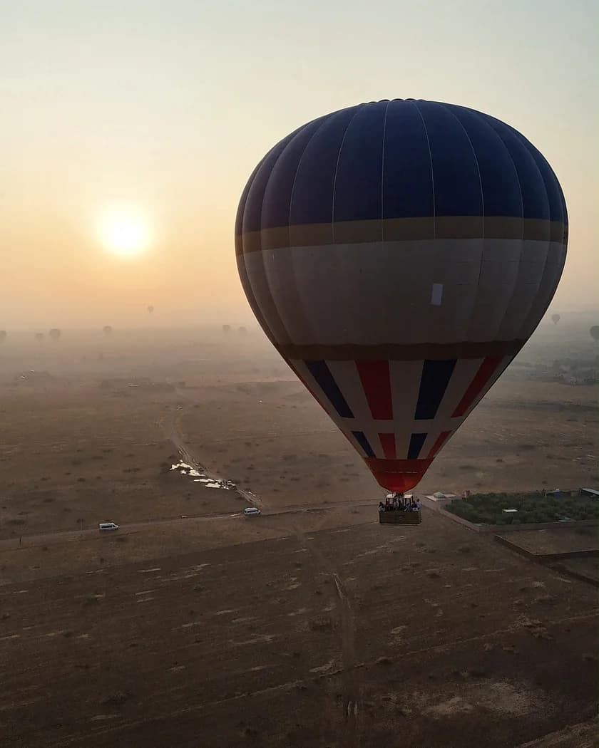 A hot-air balloon above the landscape with the rising sun to its left