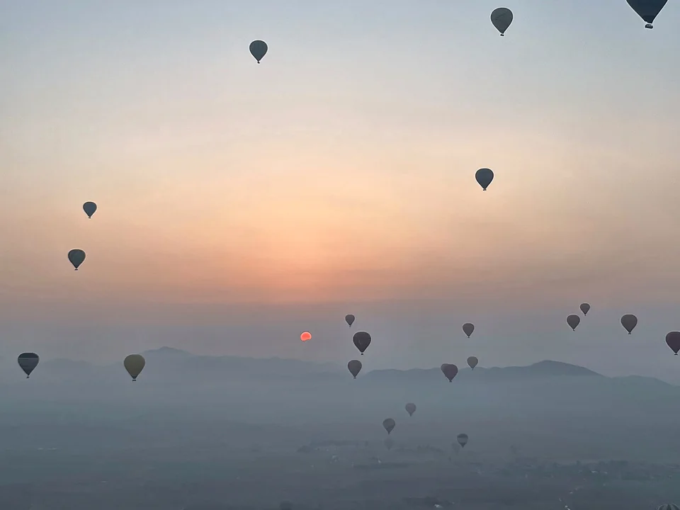 Hot-air balloons scattered across a hazy sky at sunrise