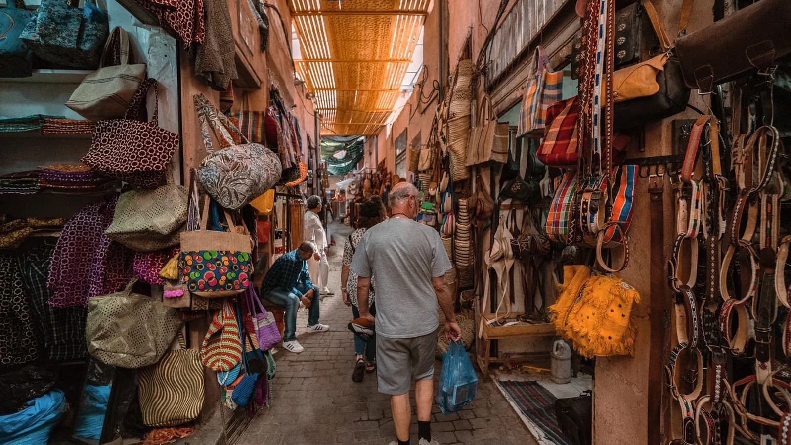 Visitors walking through a covered Marrakech souk lined with bags and craft stalls